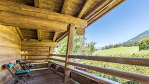 Une terrasse en bois avec une rambarde, des bancs en bois et une vue sur un paysage verdoyant.