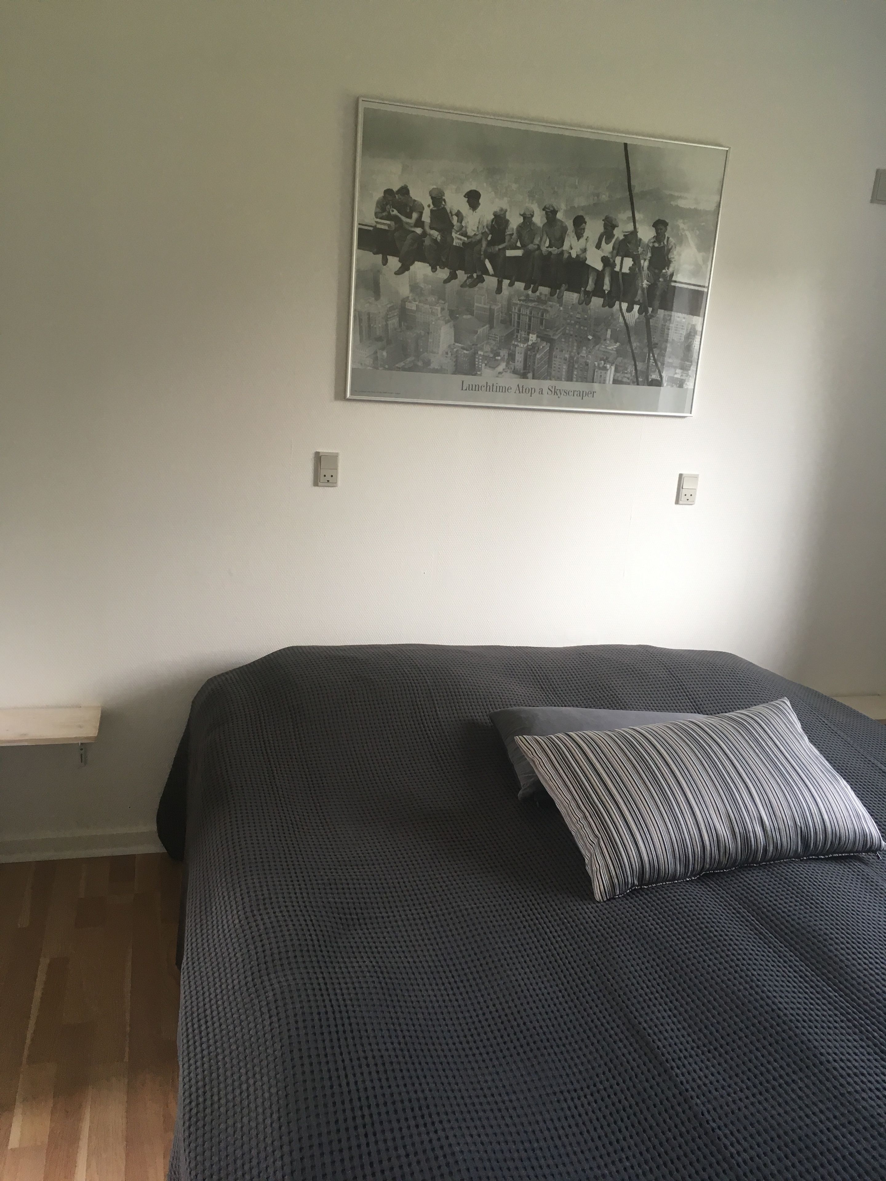A bedroom with a bed, a pillow, a framed picture on the wall, and a wooden floor.