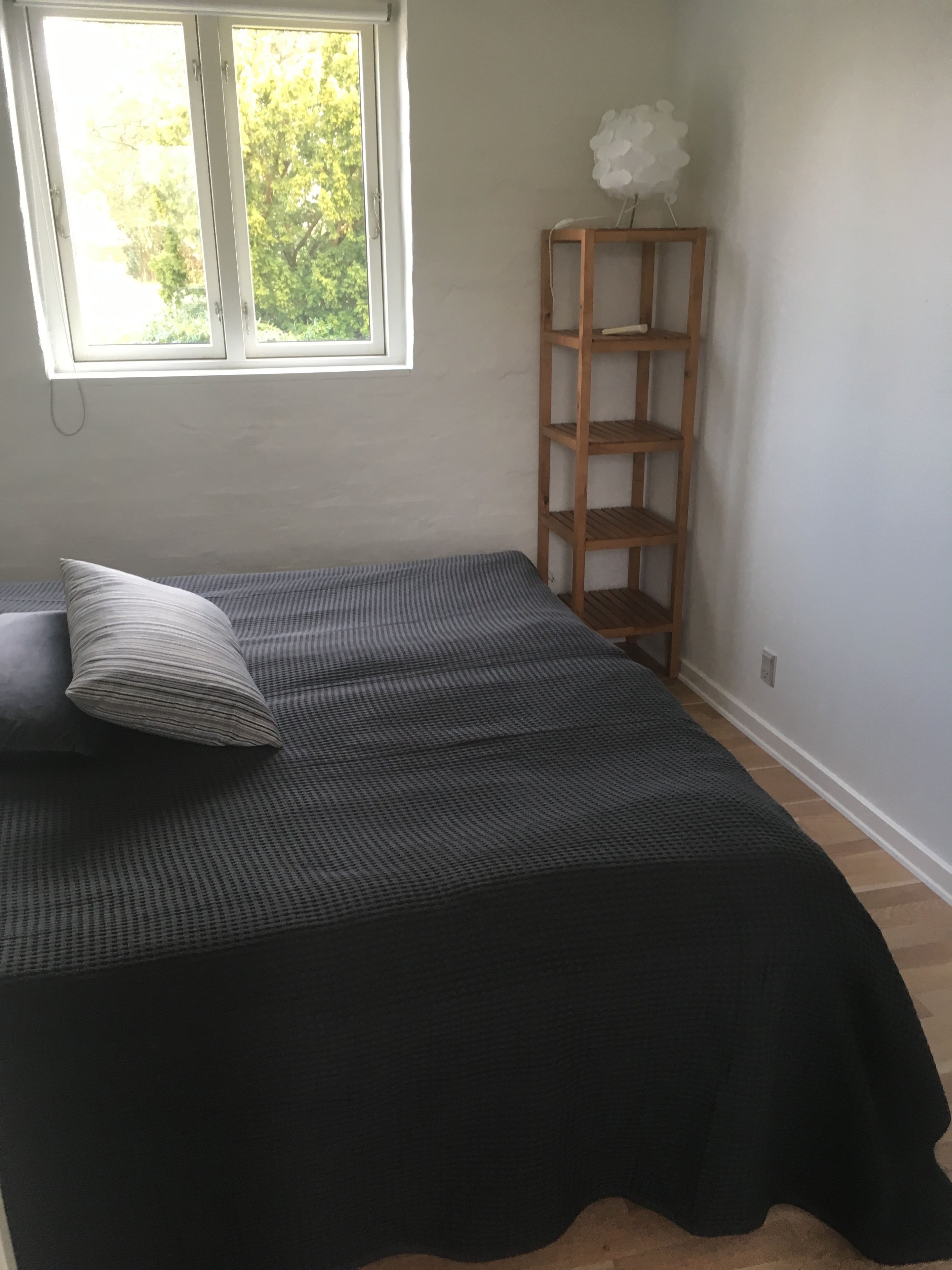 Un dormitorio con una cama, una ventana y un estante de madera.