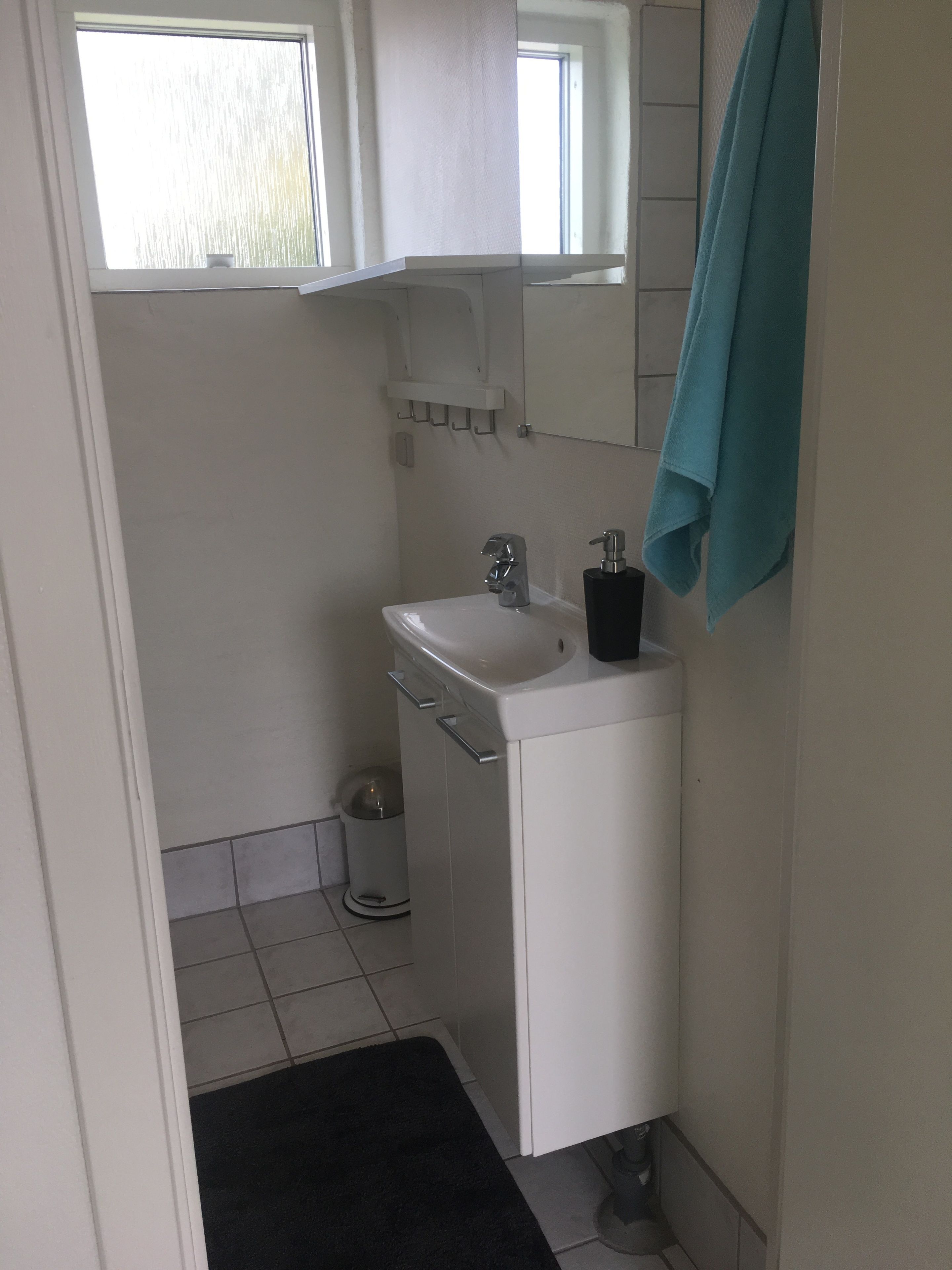 Une petite salle de bain propre, avec un lavabo blanc, un miroir et une serviette accrochée au mur.