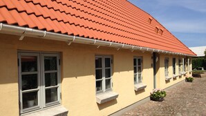 A yellow building with a red tiled roof, multiple windows with stone sills, and a cobblestone courtyard. - Birkende Bed And Breakfast (Langeskov)