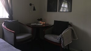 A small, dimly lit room with two armchairs, a small table with a plant, and two framed pictures on the wall. - Birkende Bed And Breakfast (Langeskov)