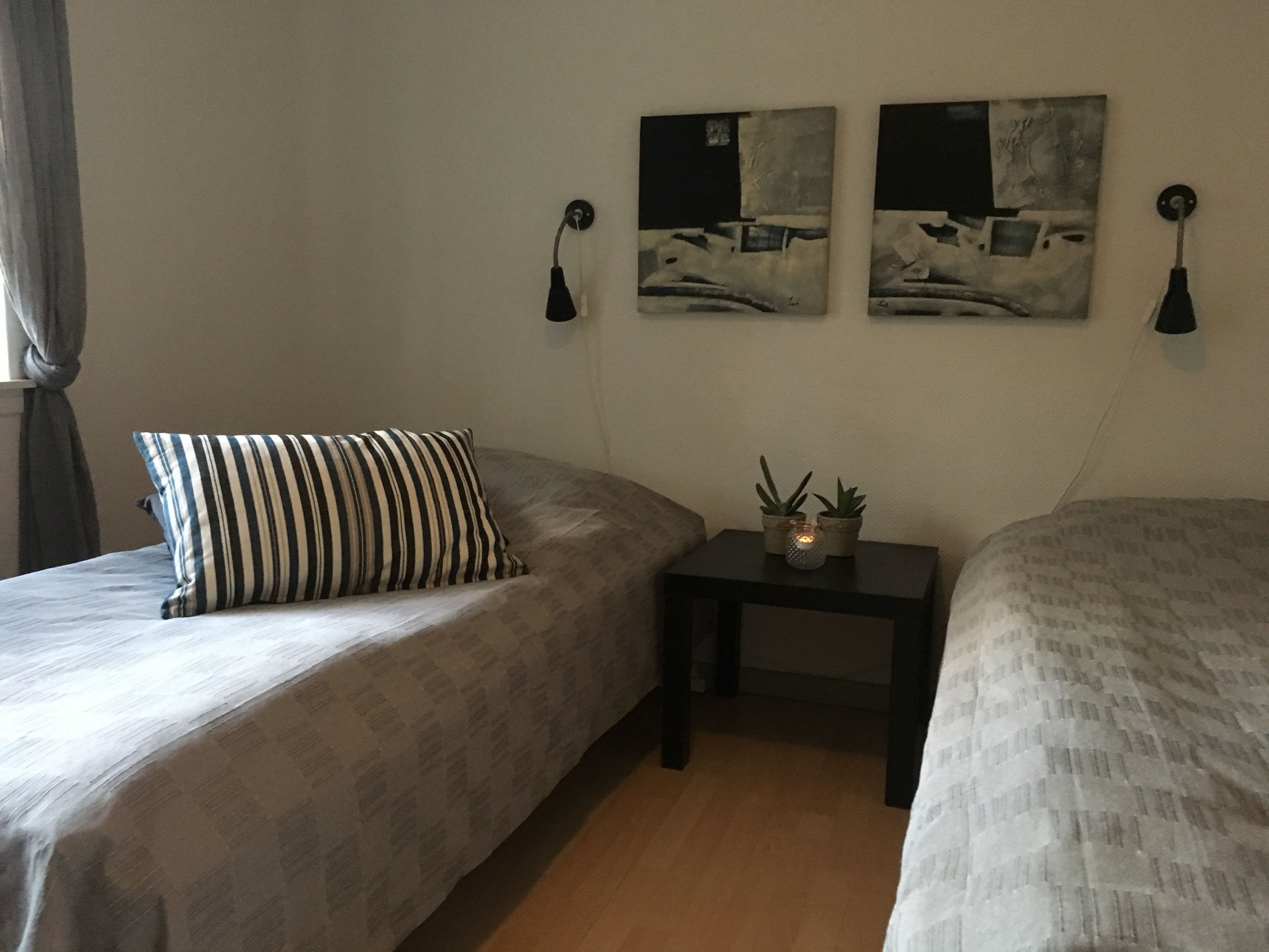 Un dormitorio con dos camas, una mesita de noche con plantas y dos lámparas de pared.