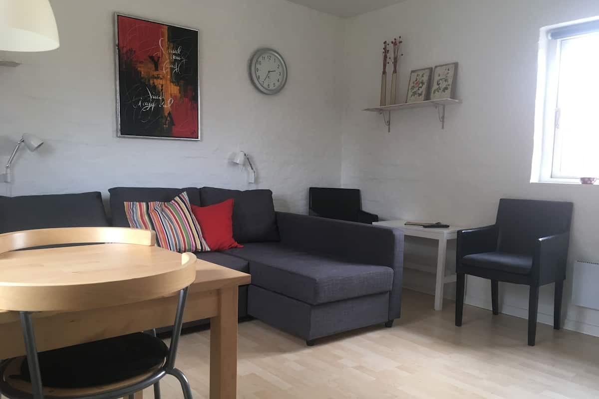 Un salon moderne avec un canapé gris, une table en bois, un fauteuil noir, une horloge blanche et un tableau encadré accroché au mur.
