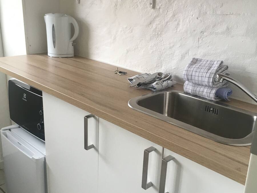 A kitchen with a wooden countertop, a stainless steel sink, a kettle, and a dish rack.