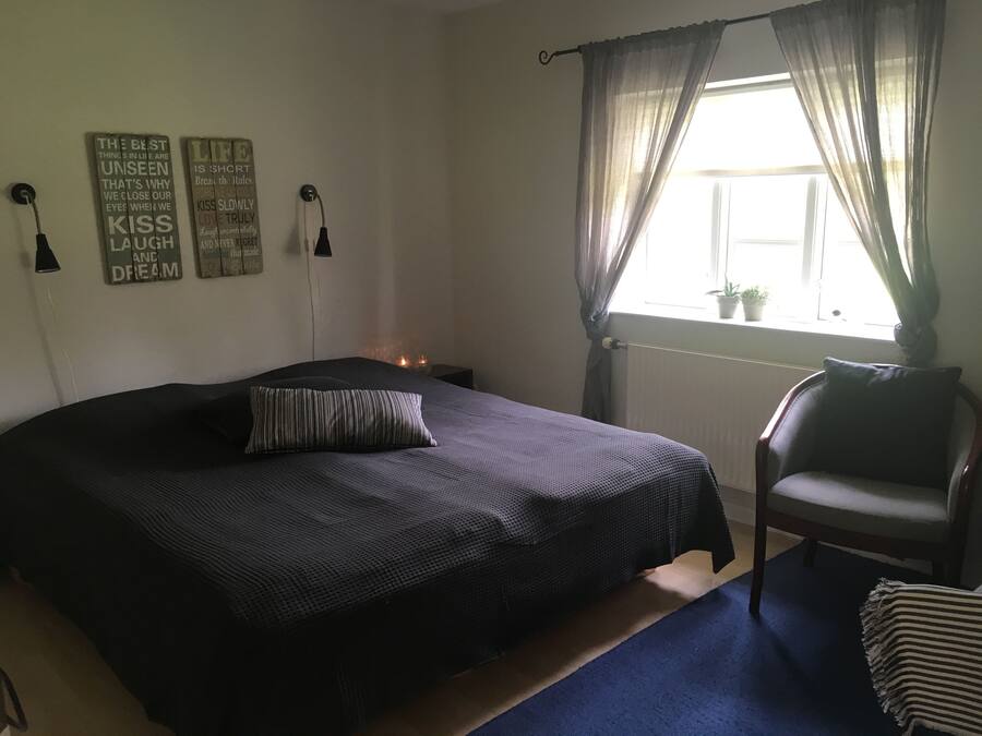 A bedroom with a large bed, a chair, a window with curtains, and motivational wall art.