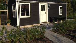 A small, single-story house with a dark exterior and white trim. It features a front door, two windows, and a small porch area. - Birkende Bed And Breakfast (Langeskov)