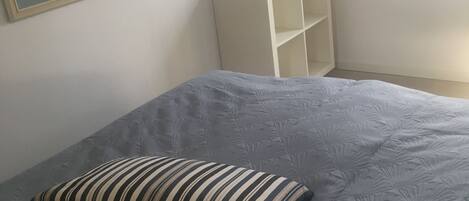 A bedroom with a bed, a framed picture on the wall, a shelf with a vase, and a window.