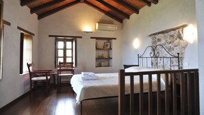 Une pièce chaleureuse avec un plafond en bois, un lit, une chaise, une table et une étagère fixée au mur, ornée d’objets décoratifs.