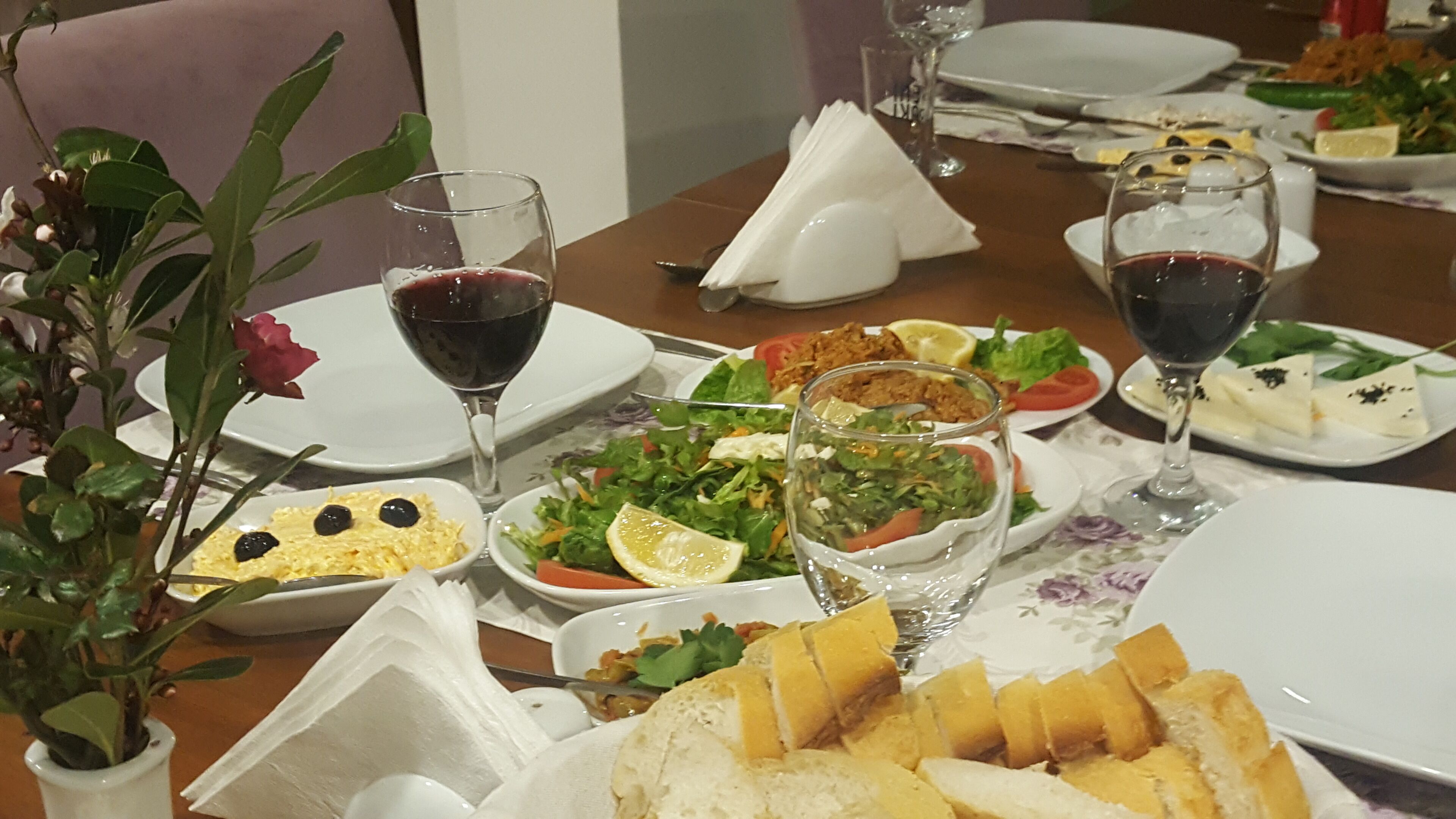 A dining table set with various dishes, including salads, bread, and a cheese platter, accompanied by wine glasses.