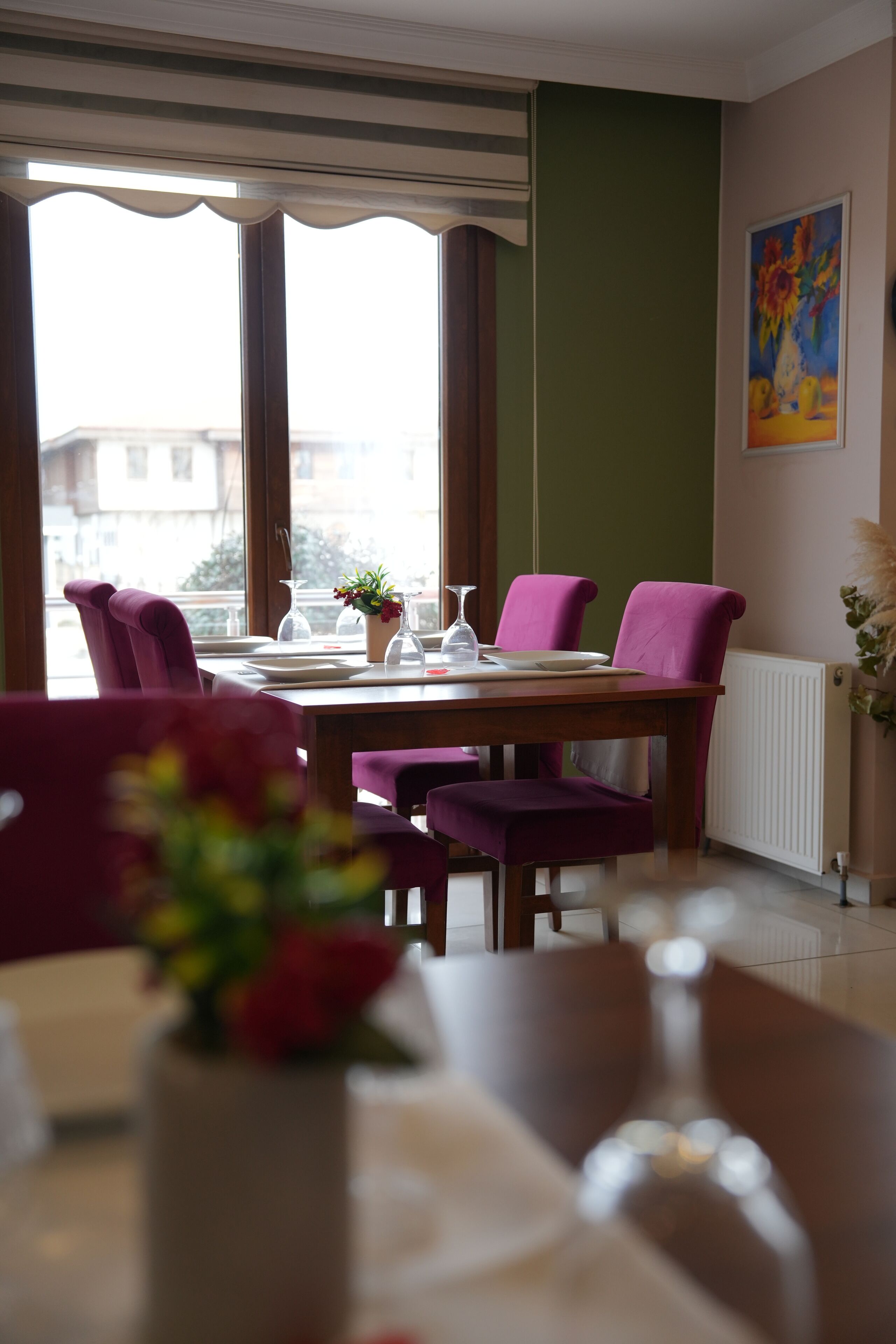 Un comedor con mesa de madera, sillas moradas, un jarrón con flores y una ventana con persianas.