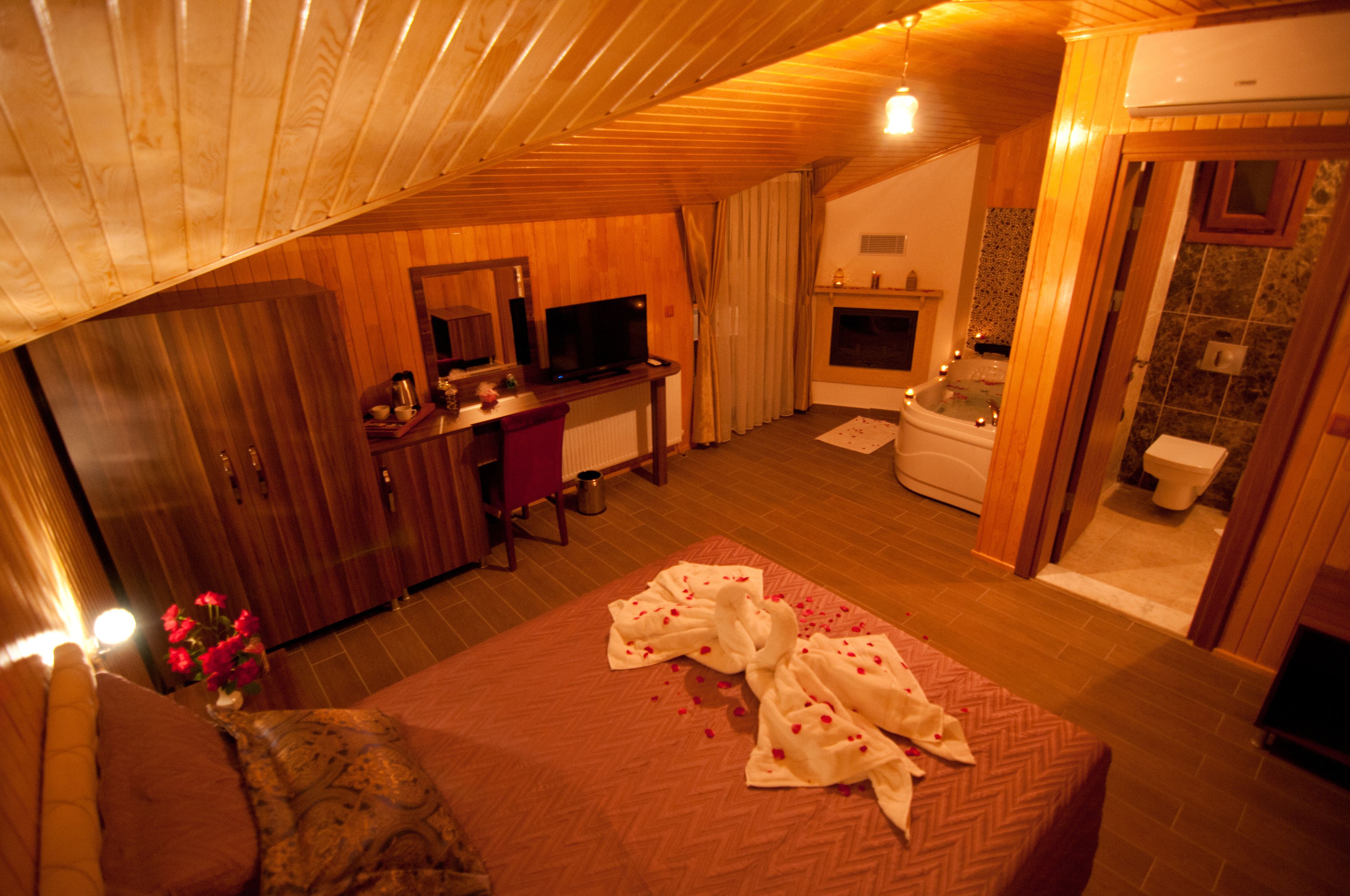 A cozy room with a bed, a desk, a TV, a fireplace, and a bathroom.