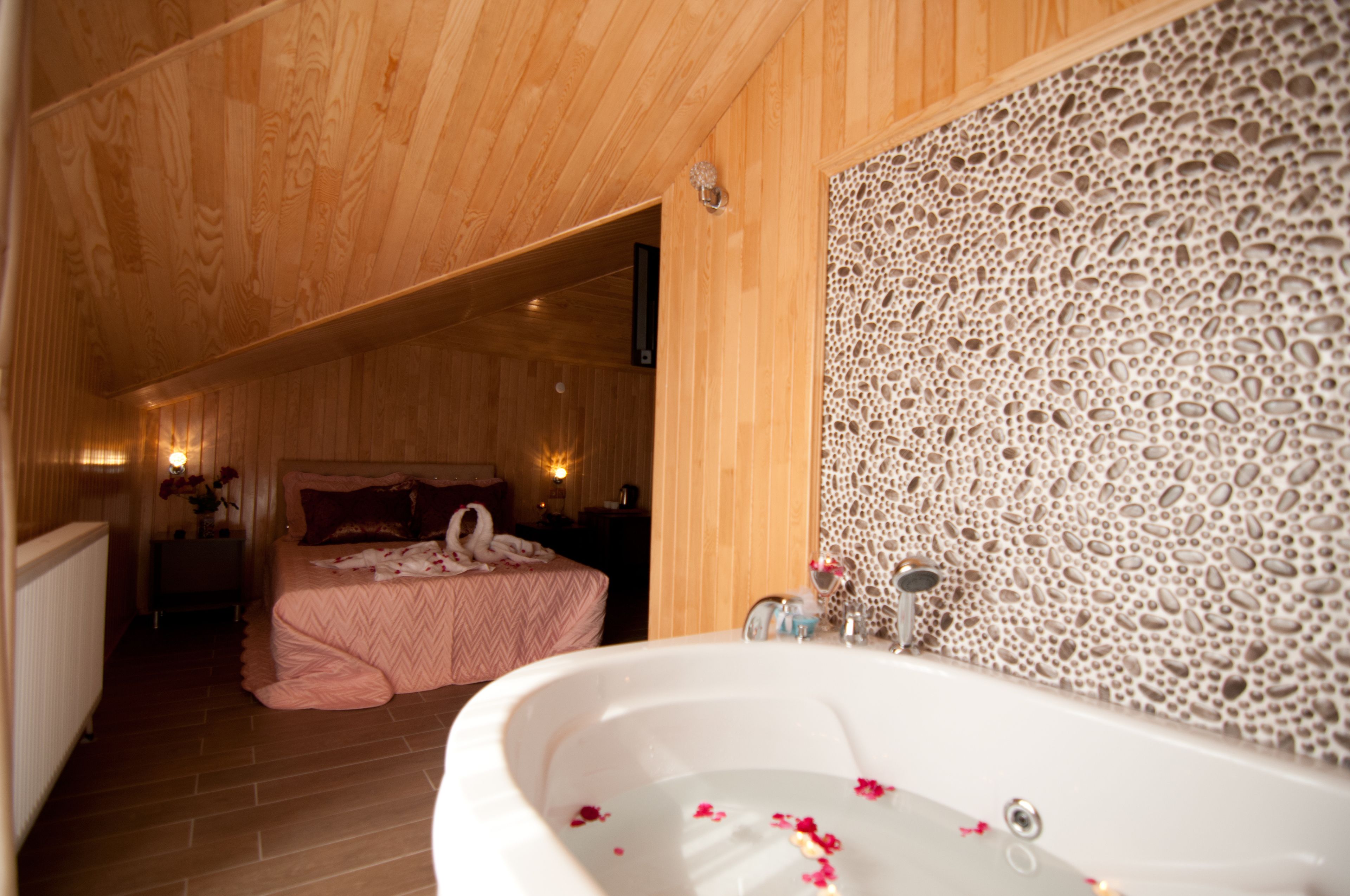 Un interior de madera con una bañera grande, una cama con ropa de cama rosa y una pared estampada.