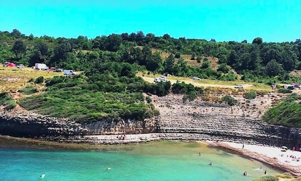 A coastal area with a beach, rocky cliffs, and a road with vehicles. - Defne Hotel (Sile)