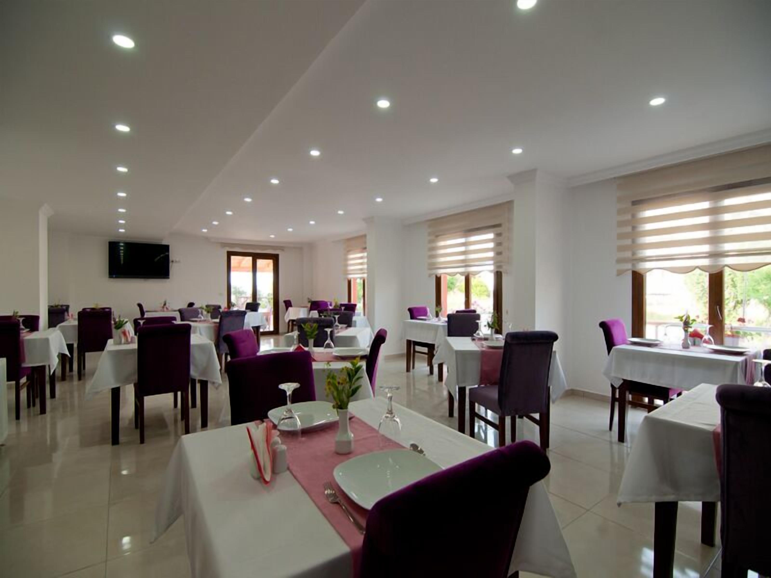 A dining area with tables set for two, white tablecloths, and purple chairs.