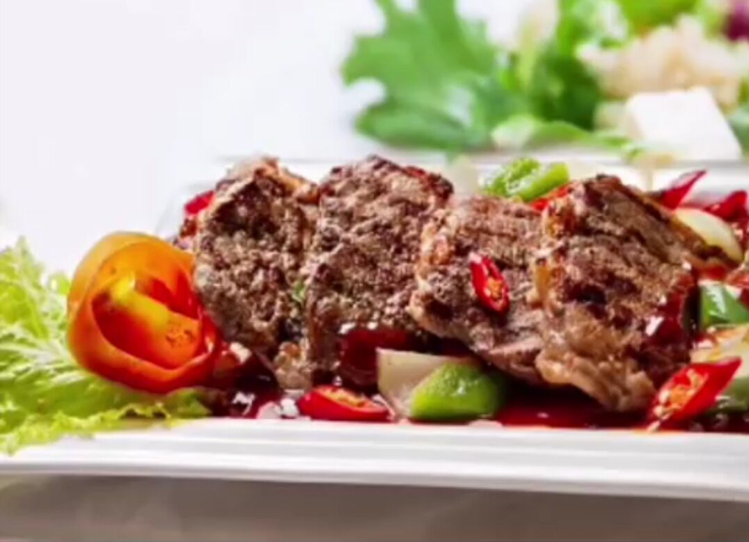 Un plat composé de viande, de légumes et d’une sauce rouge, servi dans une assiette blanche.
