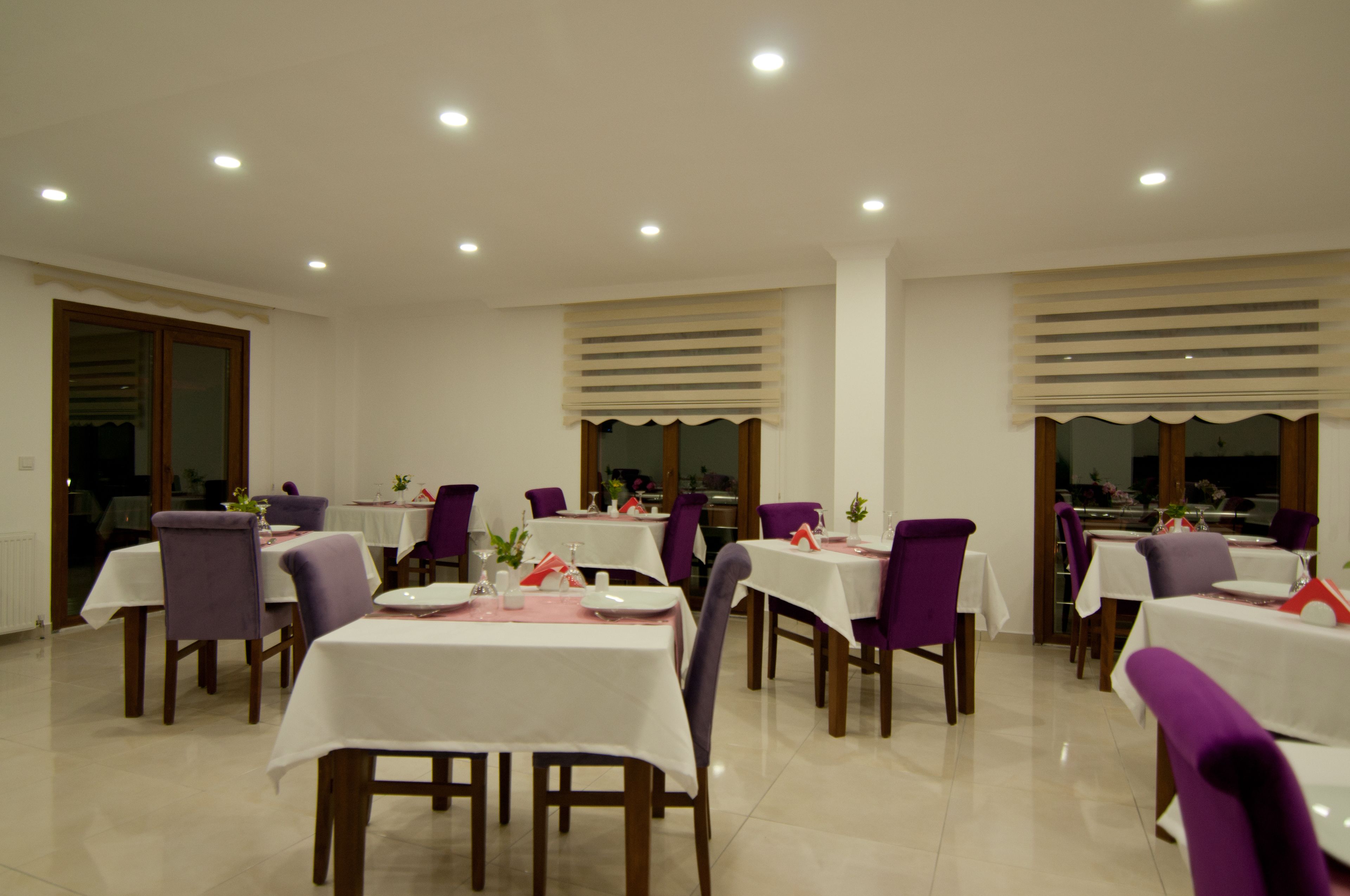A dining area with multiple tables and chairs, each set with white tablecloths and purple chairs.