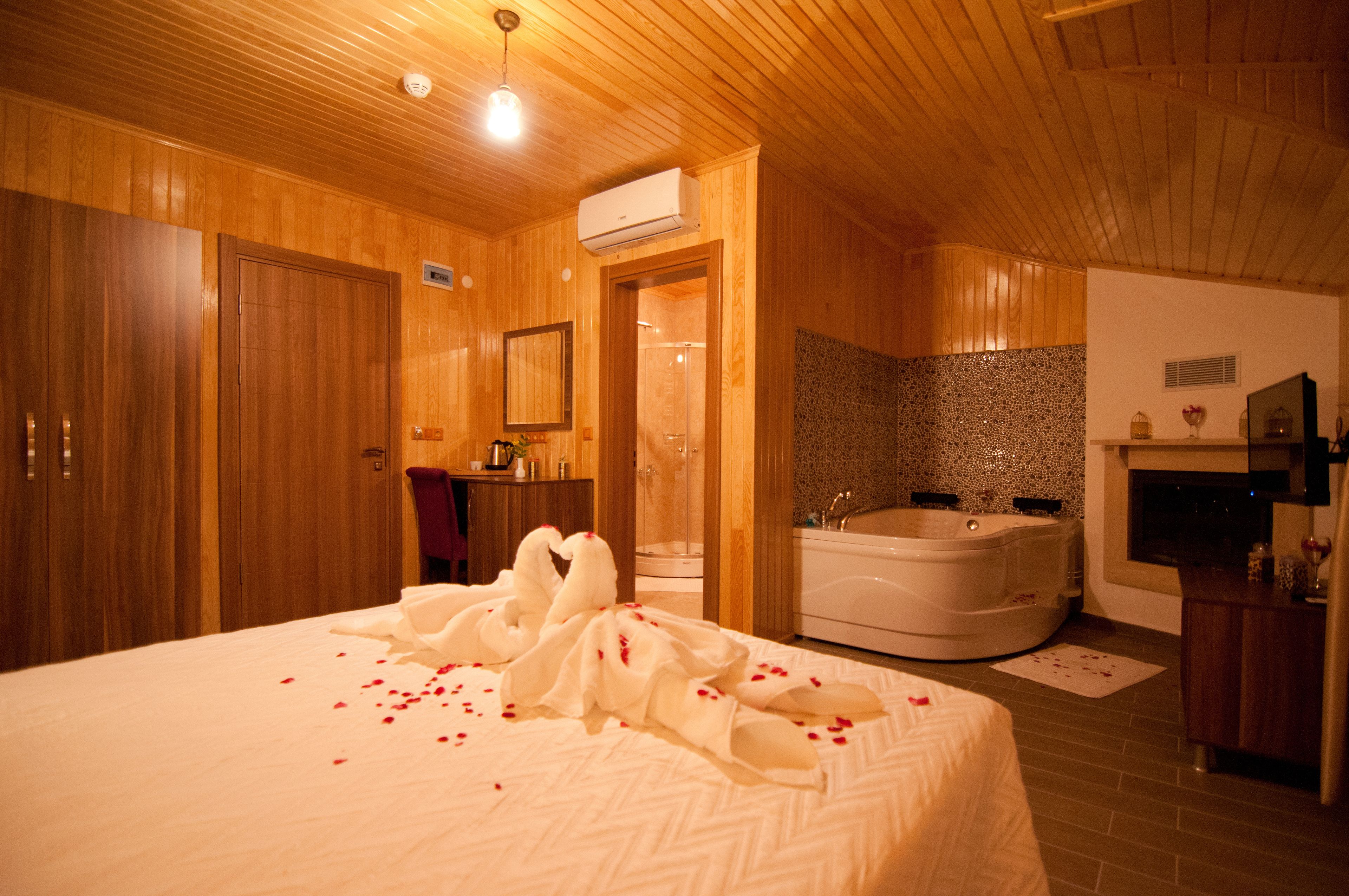 A wooden-finished bedroom with a large bed, a bathroom with a bathtub, and a shower.