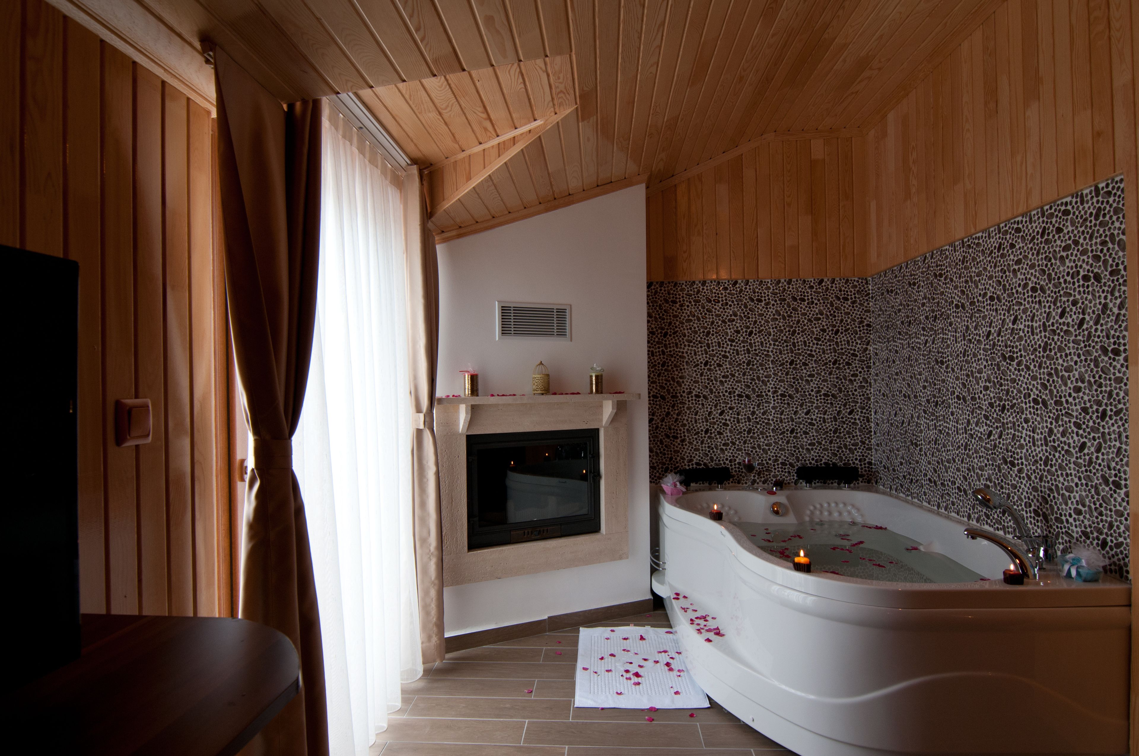 Una habitación con techo de madera, chimenea, bañera grande con pétalos de rosa y pared de piedra.