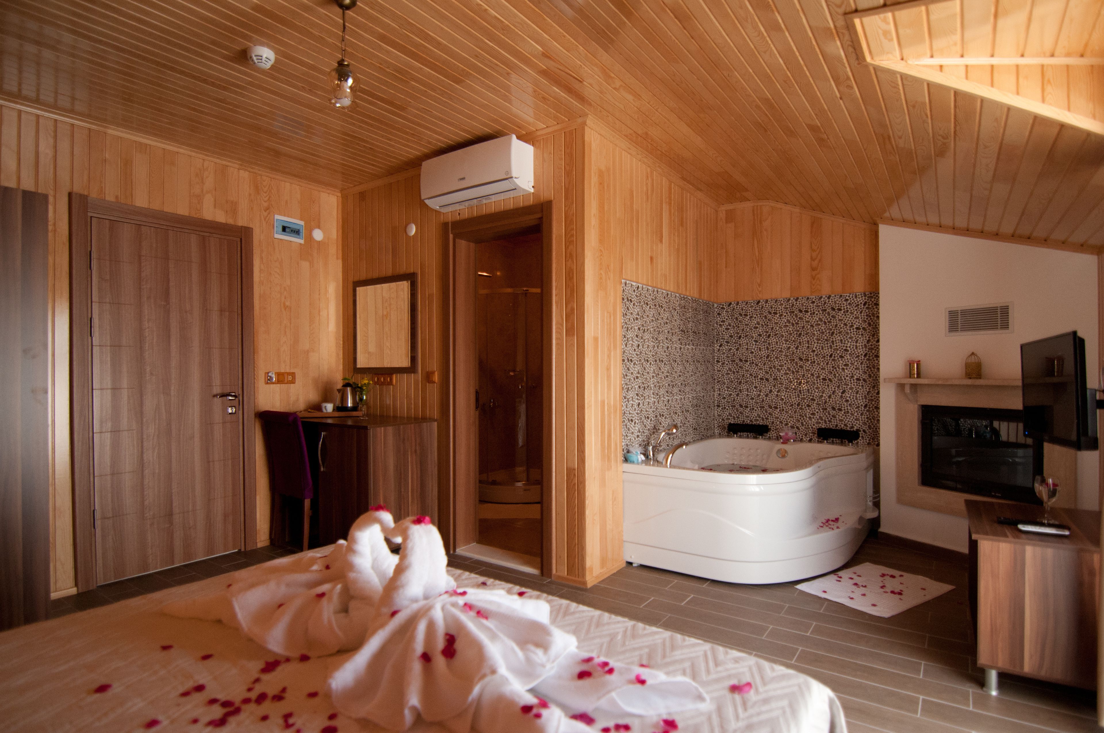 A wooden-finished bedroom with a large bed, a bathtub, and a TV.