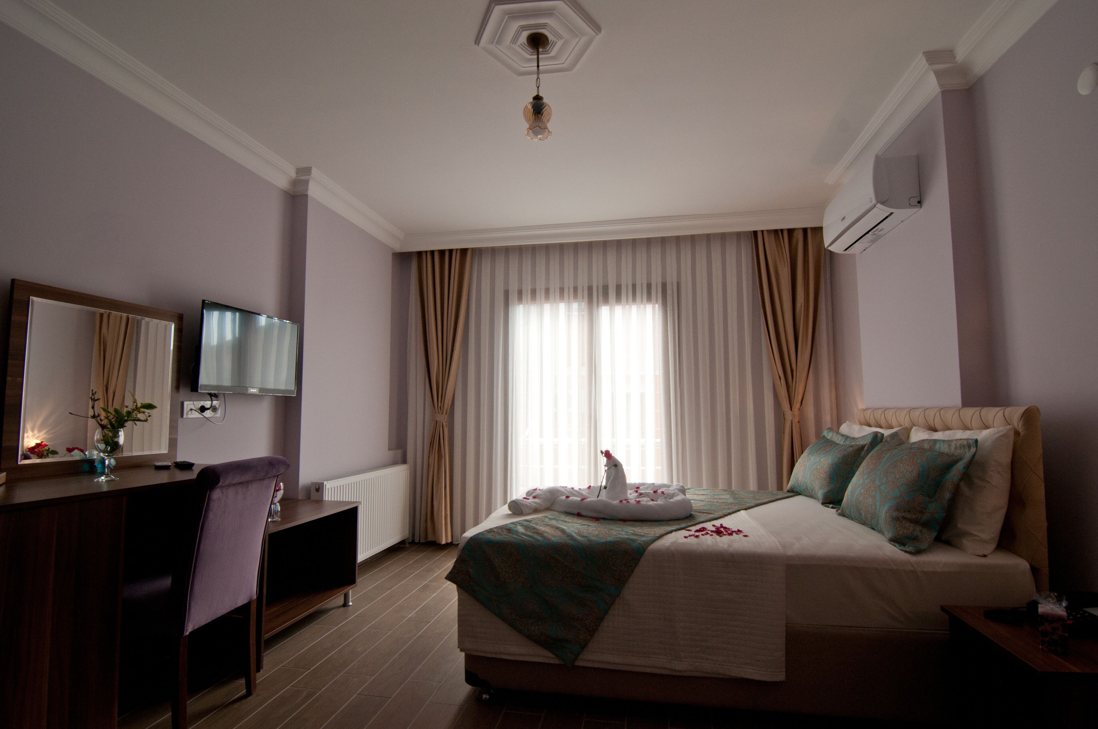 Habitación de hotel con cama, escritorio, silla, espejo, televisor y ventana con cortinas.