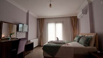 Habitación de hotel con cama, escritorio, silla, espejo, televisor y ventana con cortinas.