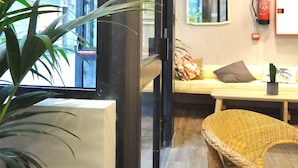 A room with a large window, a wicker chair, a white sofa, and a small table. - Quartier Bilbao Hostel (Bilbao)