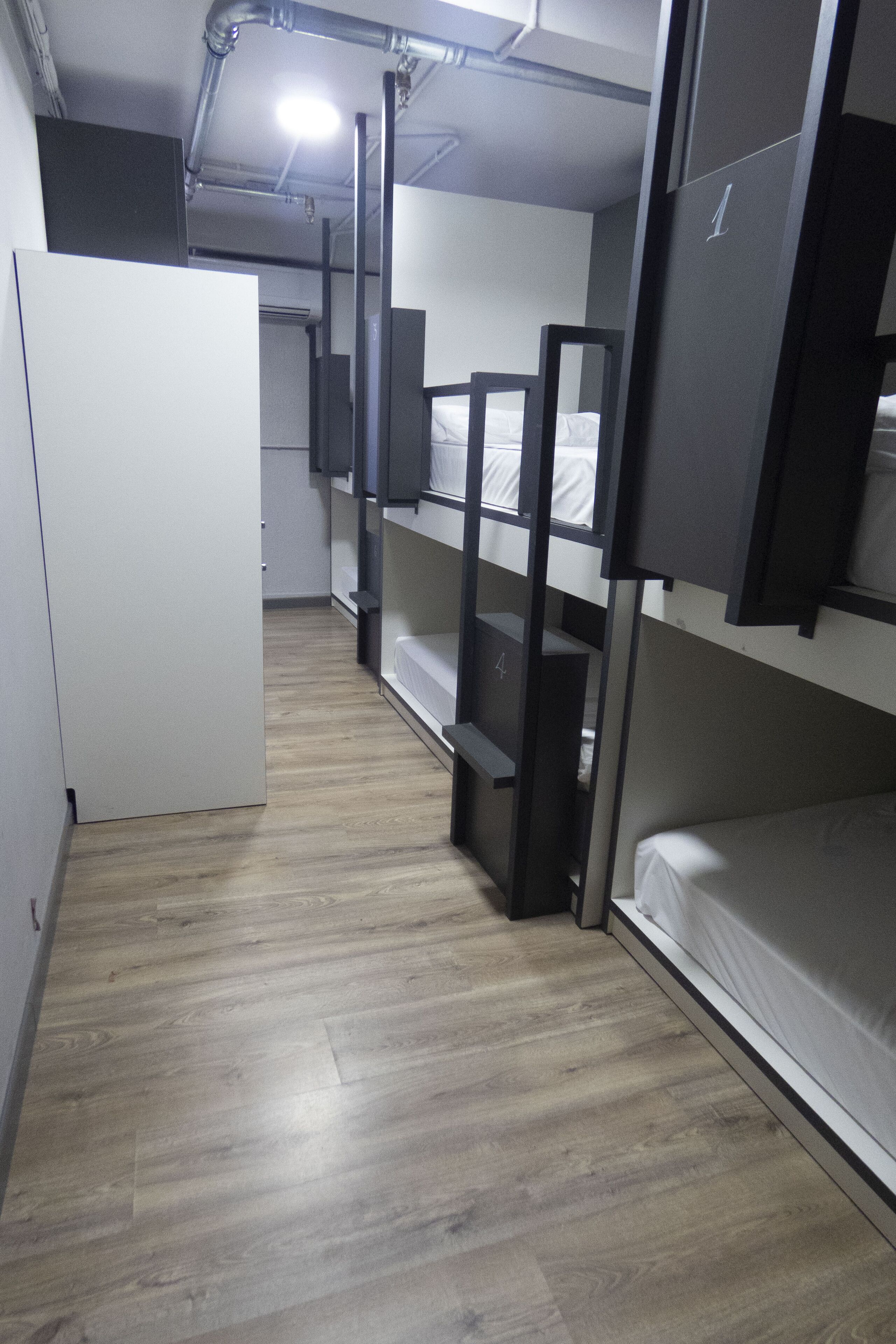 A dormitory room with bunk beds, a white wardrobe, and a wooden floor.