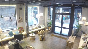 A cozy interior with seating areas, a reception desk, and large windows offering views of the street. - Quartier Bilbao Hostel (Bilbao)