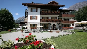 A multi-story hotel with balconies, outdoor seating, and a mountainous backdrop. - Meuble Cima Bianca Garni (Bormio)