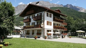 A multi-story hotel with balconies, outdoor seating, and a mountainous backdrop. - Meuble Cima Bianca Garni (Bormio)