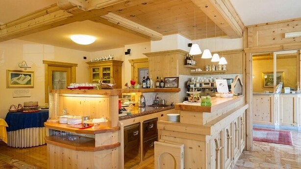 A wooden interior with a bar area, wooden cabinets, and a dining table with a blue tablecloth. - Meuble Cima Bianca Garni (Bormio)