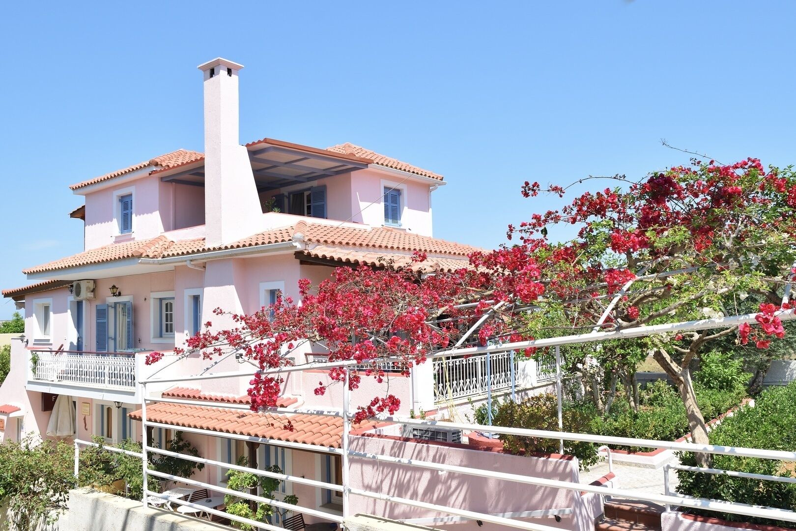 Un bâtiment à deux étages, doté d’un toit recouvert de tuiles, d’un balcon avec une balustrade blanche et d’une cheminée.