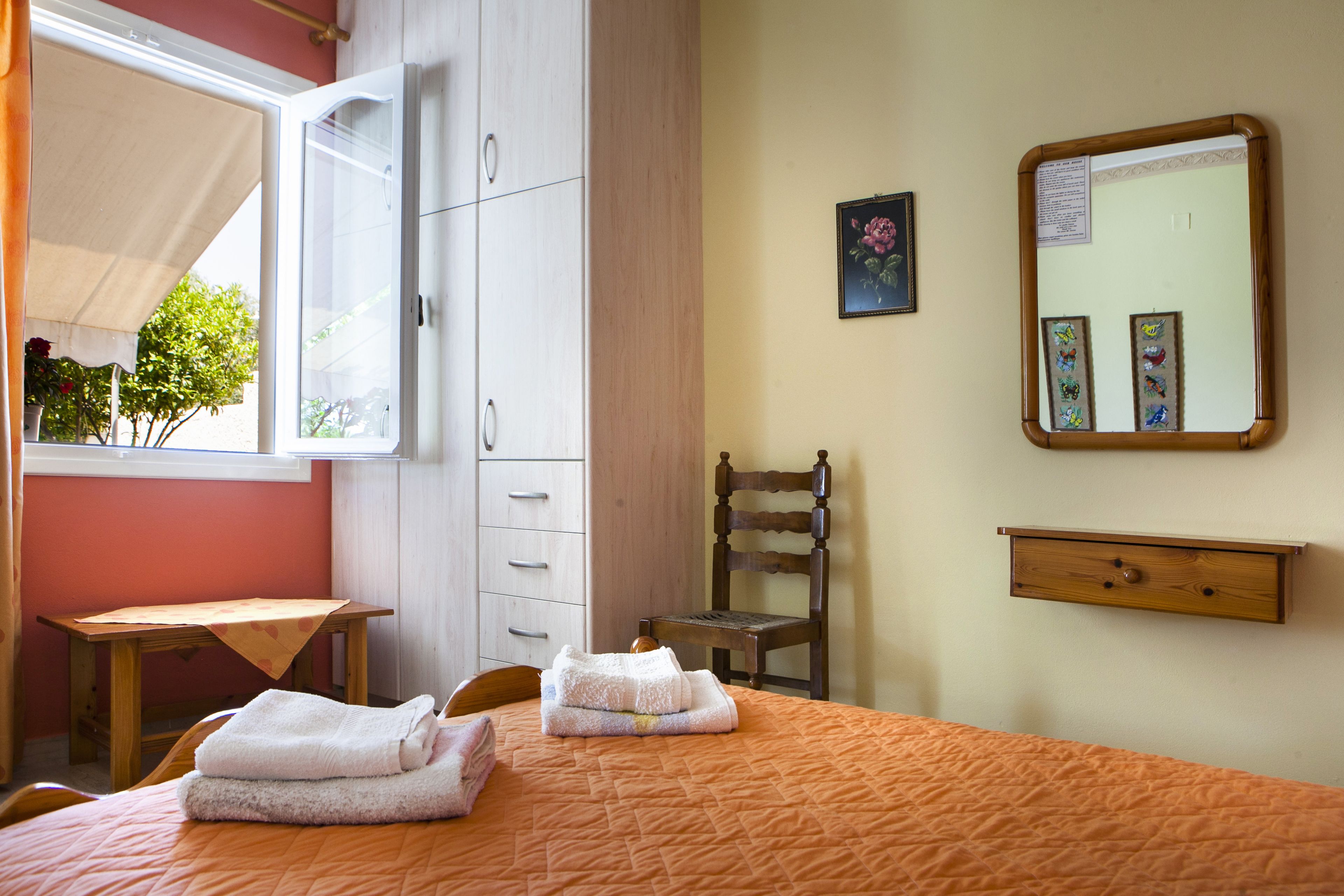 A bedroom with a bed, a wooden chair, a desk, and a wardrobe.