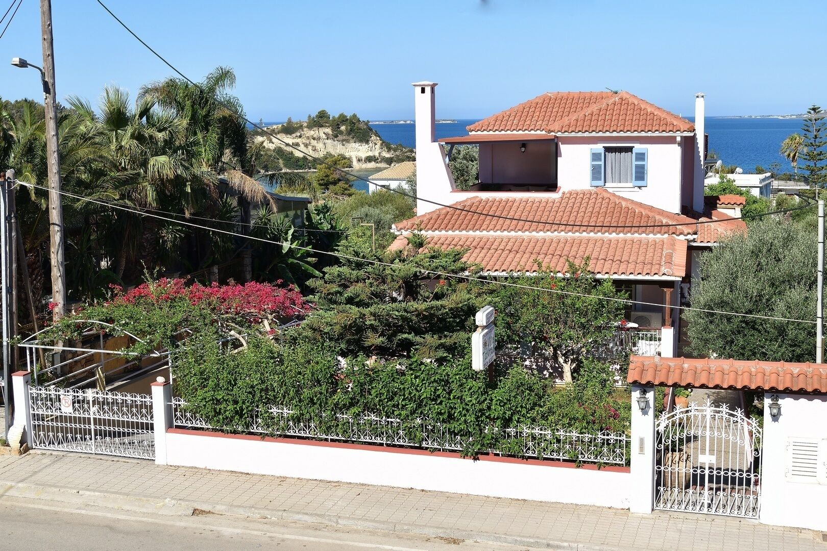 A two-story house with a red-tiled roof, a balcony, and a view of the sea.