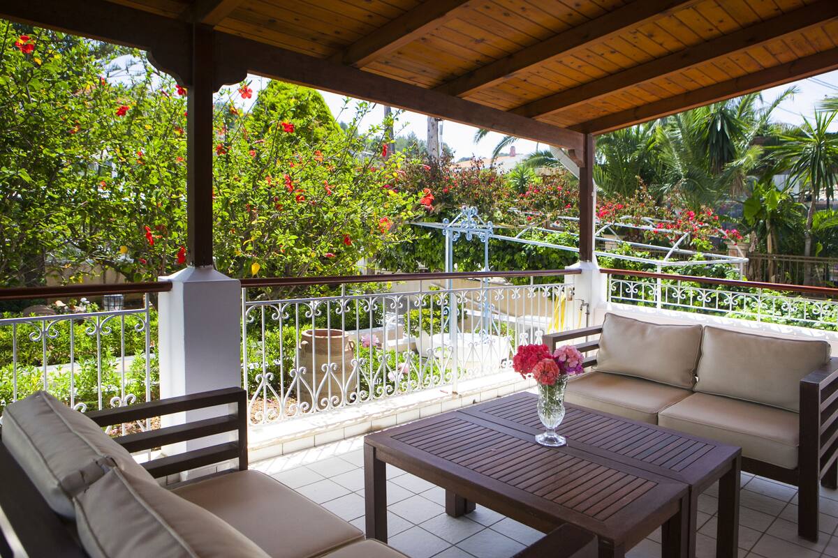 Eine überdachte Terrasse mit einem Holztisch, zwei Sofas und einem dekorativen Metallzaun.