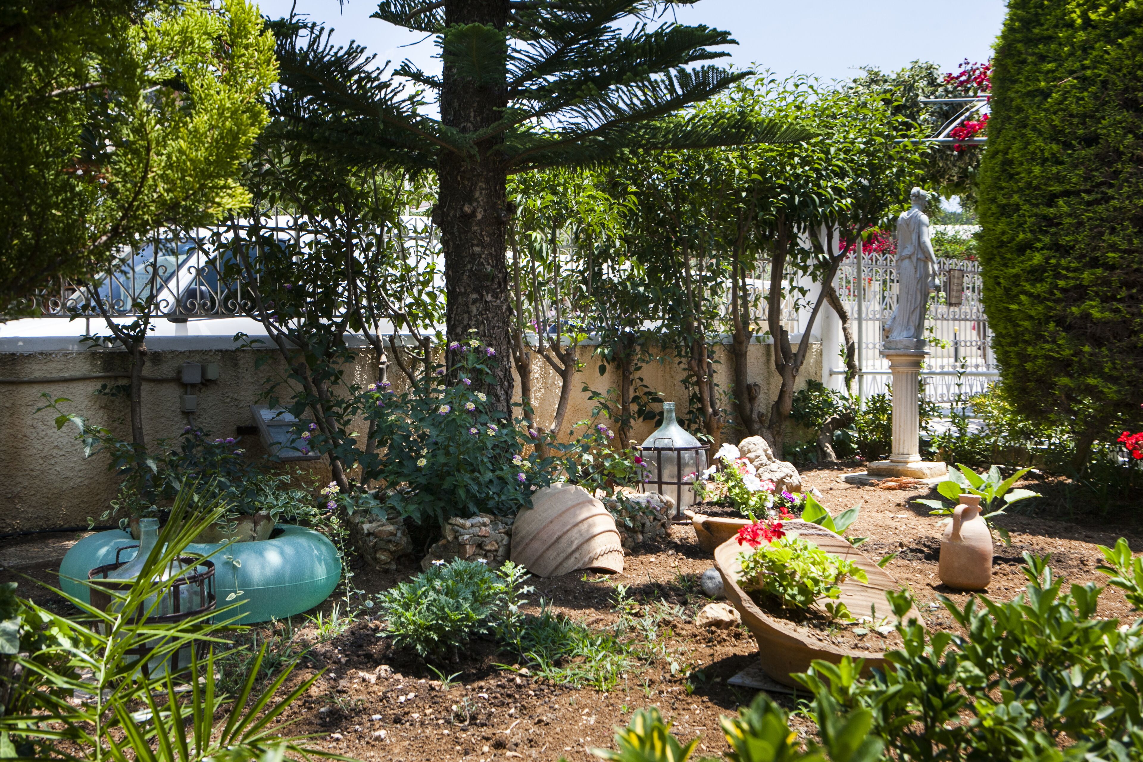 A garden with a statue, stone planters, and a fence.
