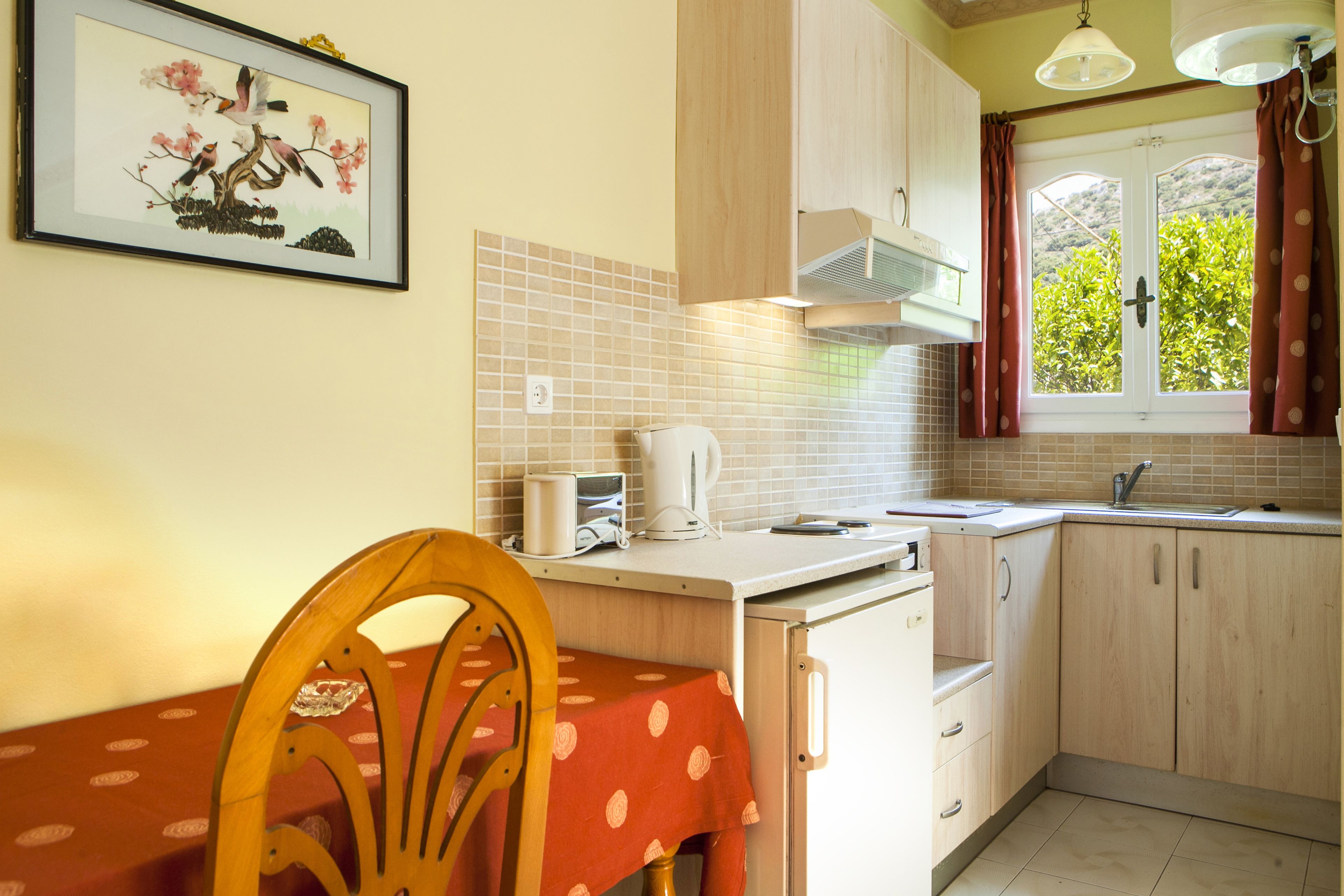 Una cocina con una mesa de comedor, sillas, un hervidor y un ventanal con cortinas.