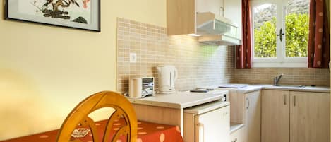 Una cocina con una mesa de comedor, sillas, un hervidor y un ventanal con cortinas.