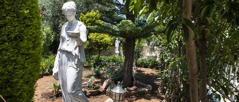 A statue in a garden with trees and a lantern.