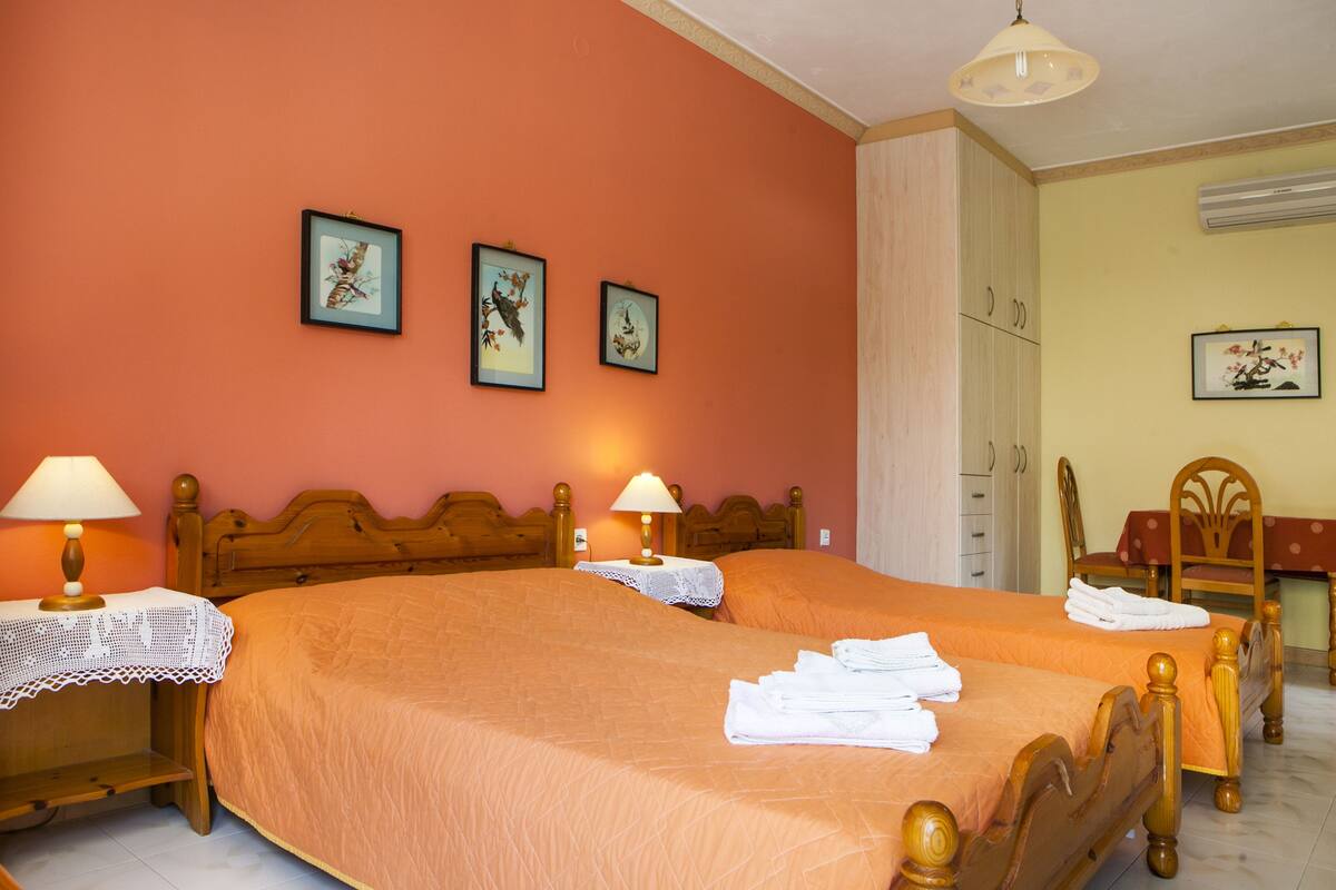 Ein Hotelzimmer mit zwei Betten, einem Holzkopfteil, einem kleinen Tisch mit Lampe und einem Sessel.