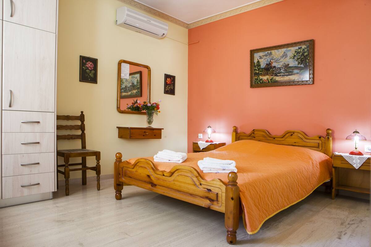 Ein Schlafzimmer mit einem hölzernen Bett, einem Nachttisch, einem Sessel, einem Kleiderschrank und einem Bild an der Wand.