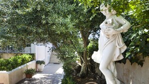 A statue in a garden with a tree and potted plants. - Tzivras Villa & Apartments (Kefalonia)
