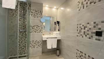 Un bany modern amb una cabina de dutxa de vidre, un lavabo amb mirall i un suport per a tovalloles.