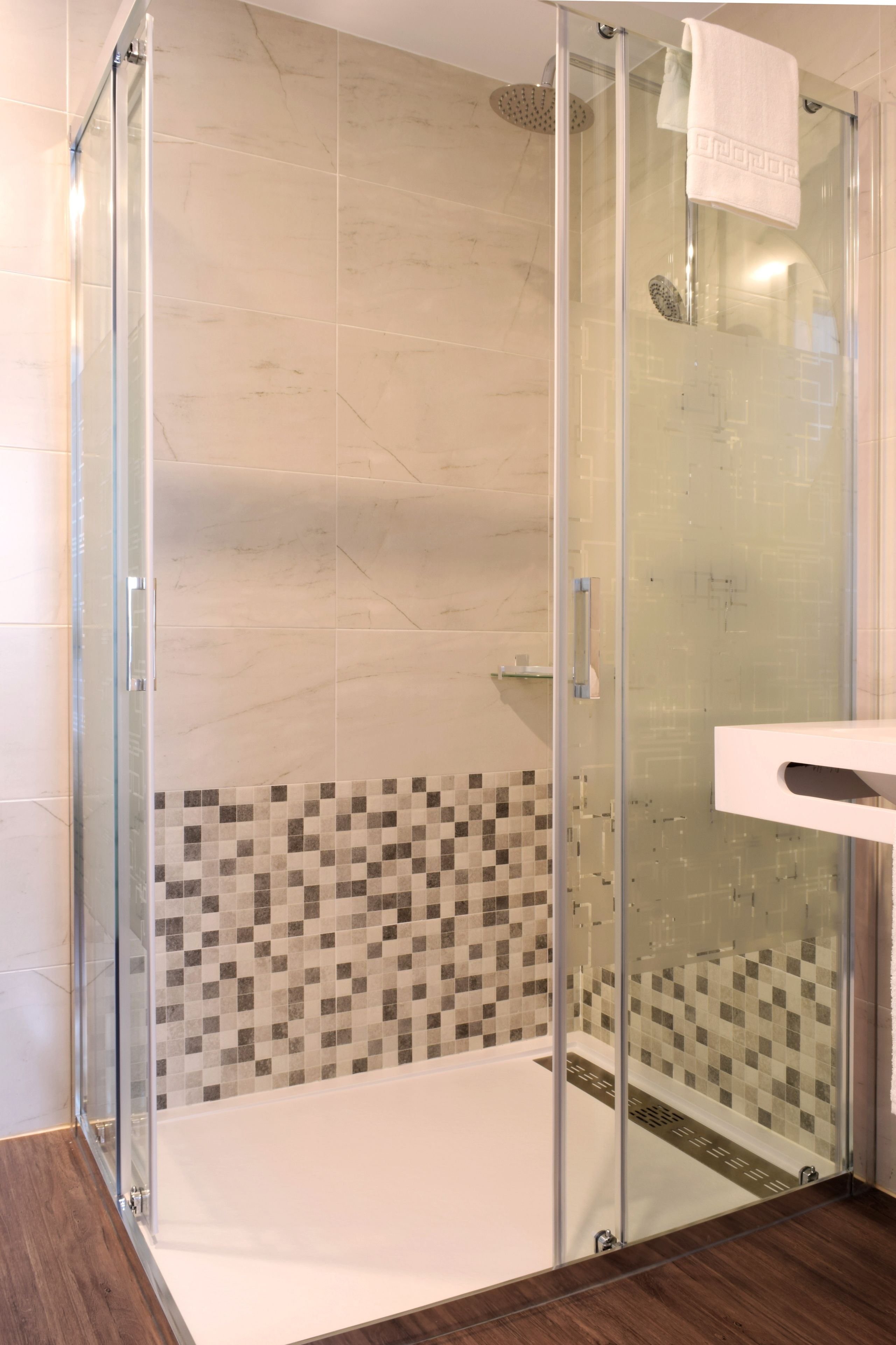 Une douche fermée par des parois de verre, avec un mur carrelé et un plancher en bois.