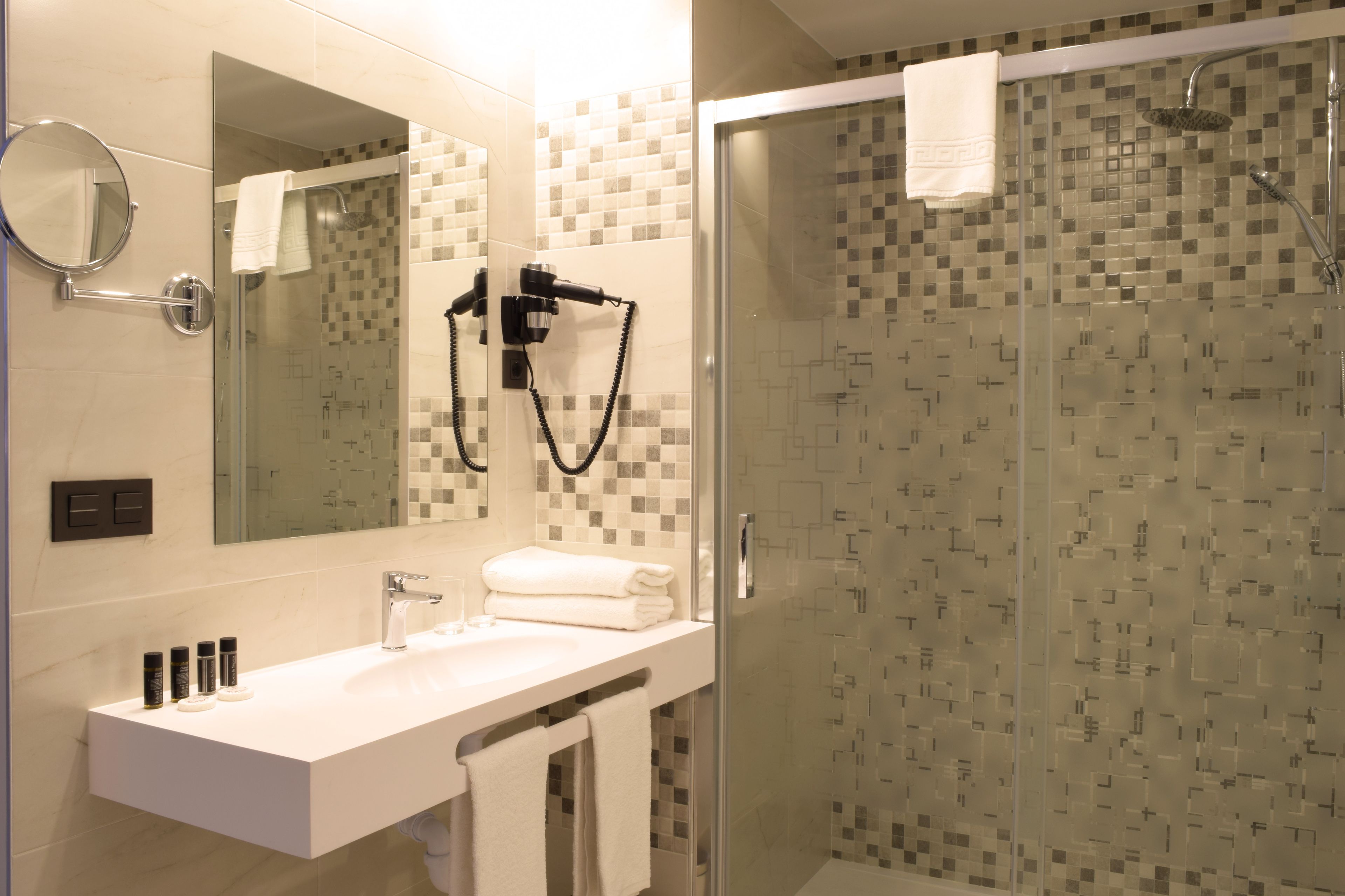 Un baño moderno con ducha de vidrio, lavamanos blanco y espejo grande.