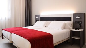 A hotel room with a large bed, a red throw blanket, two bedside tables with lamps, and a telephone. - Hotel New Bilbao Airport (Derio)