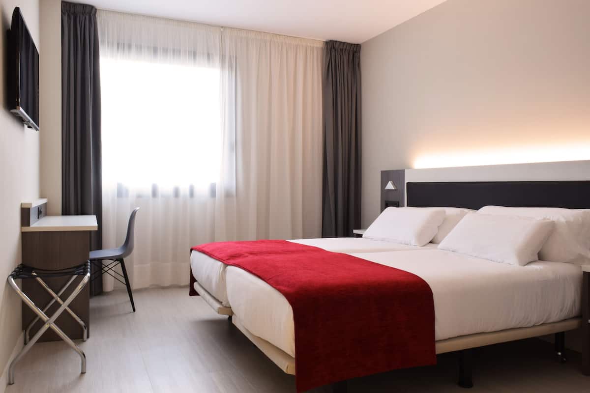 Una habitación de hotel con una cama, un escritorio, una silla y un televisor.