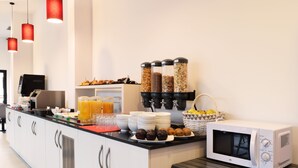 A breakfast bar with a microwave, juice dispensers, and various food items. - Hotel New Bilbao Airport (Derio)