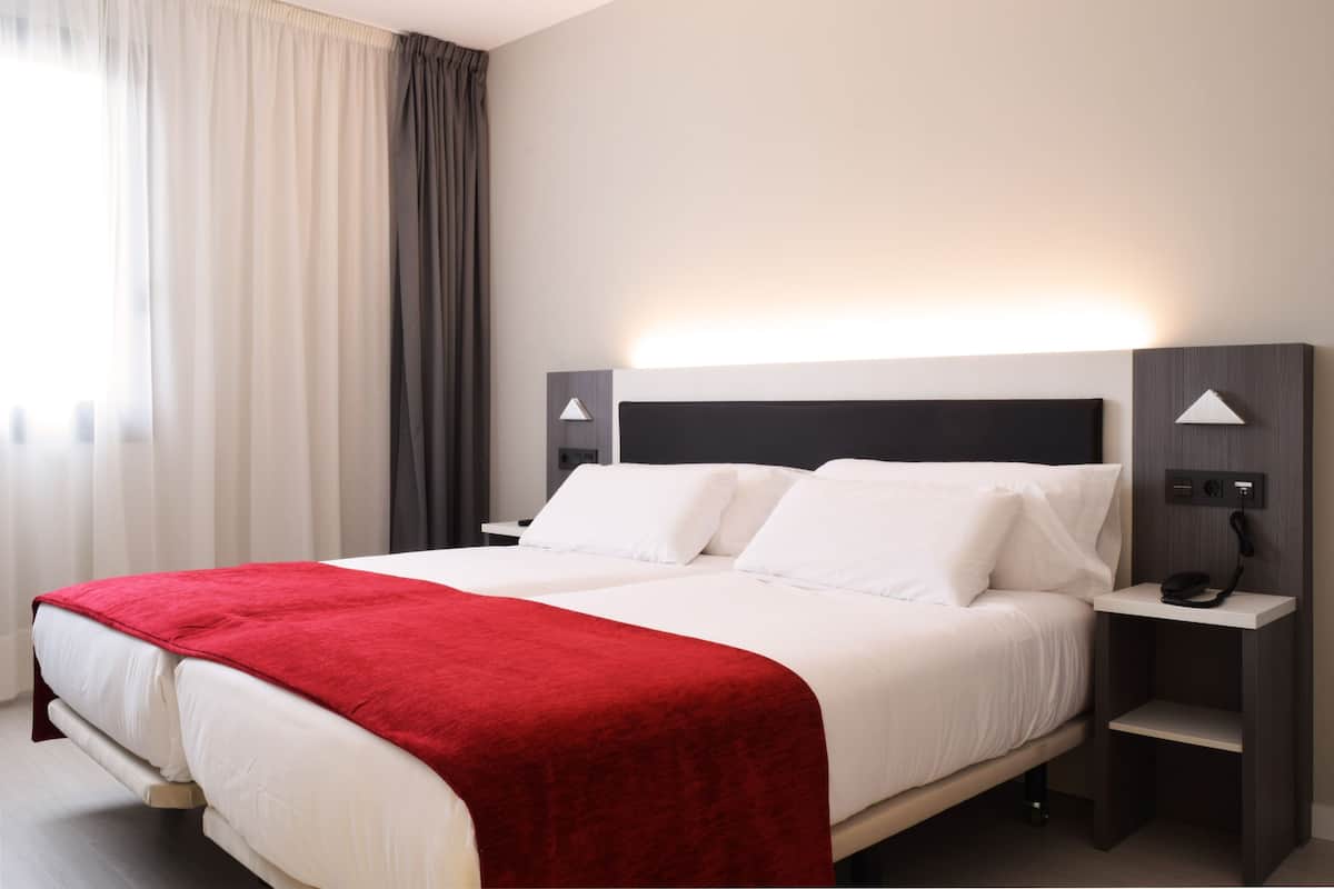 Una habitación de hotel con una cama, un edredón rojo, dos mesitas de noche con lámparas y un teléfono.